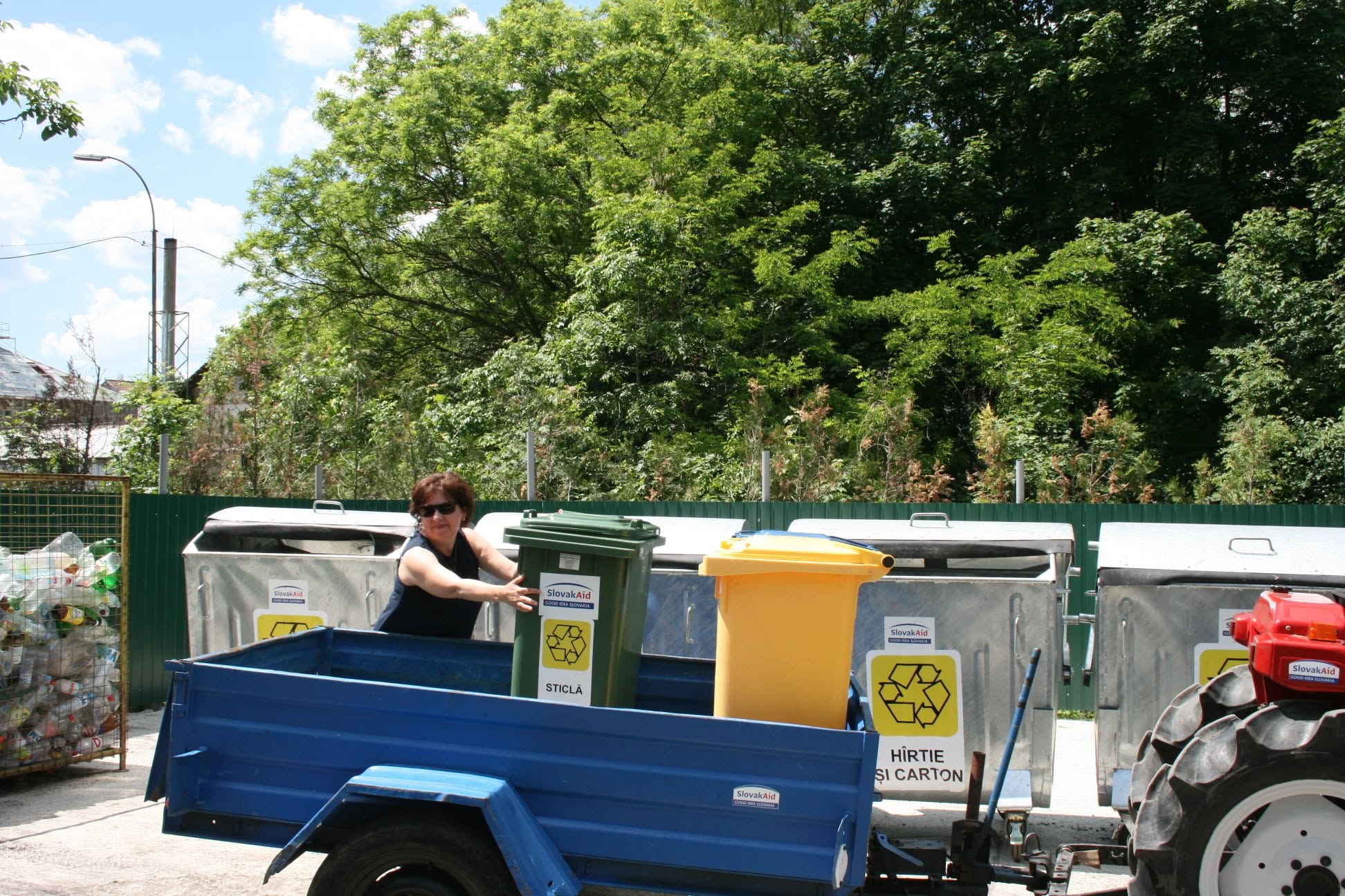 Separate waste-collection containers and a small utility trailer beside a green area in Bălți